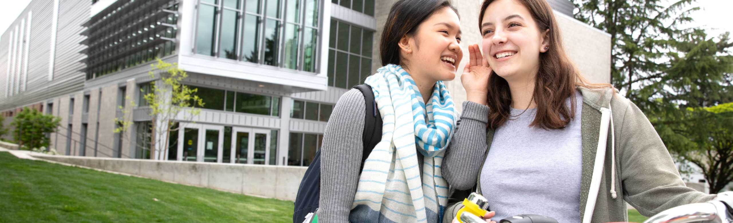 Young person smiling and whispering into the ear of another young person