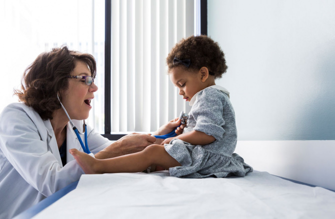 Doctor holding stethoscope up to child