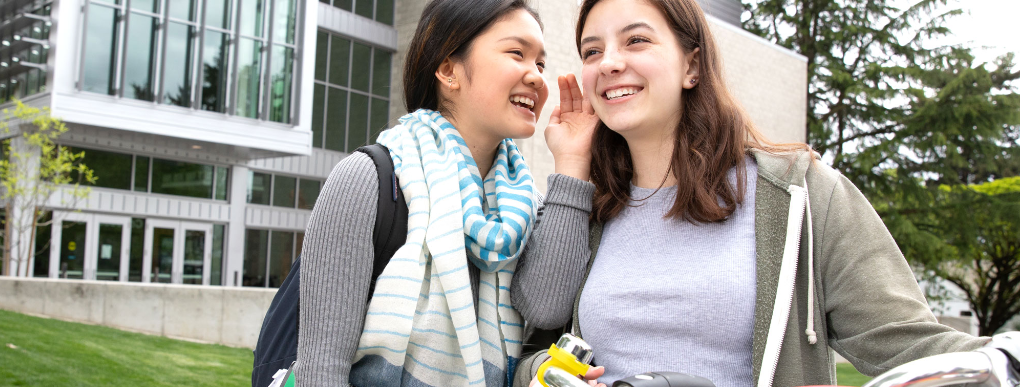 Young person smiling and whispering into the ear of another young person